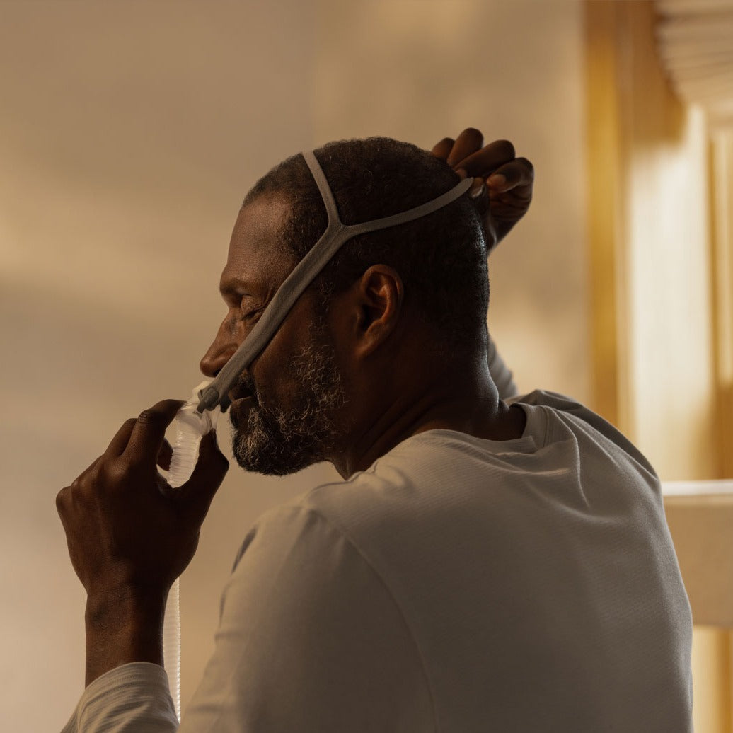 Man seen from the side wearing the AirFit P10, pulling the headgear back while the pillows sit at his nose