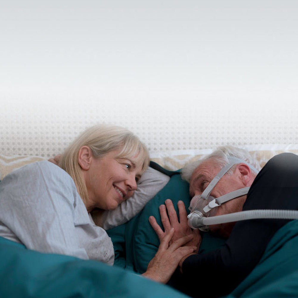 Couple lying close in bed, the man wearing an AirFit F30 mask held in place by its grey headgear