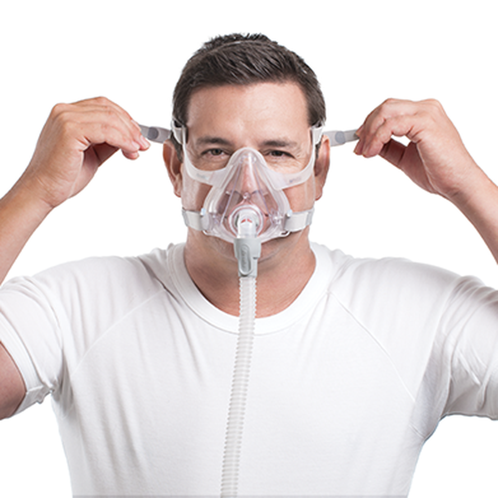 Man pulling the AirFit F10 headgear over his head while holding the full face mask in place