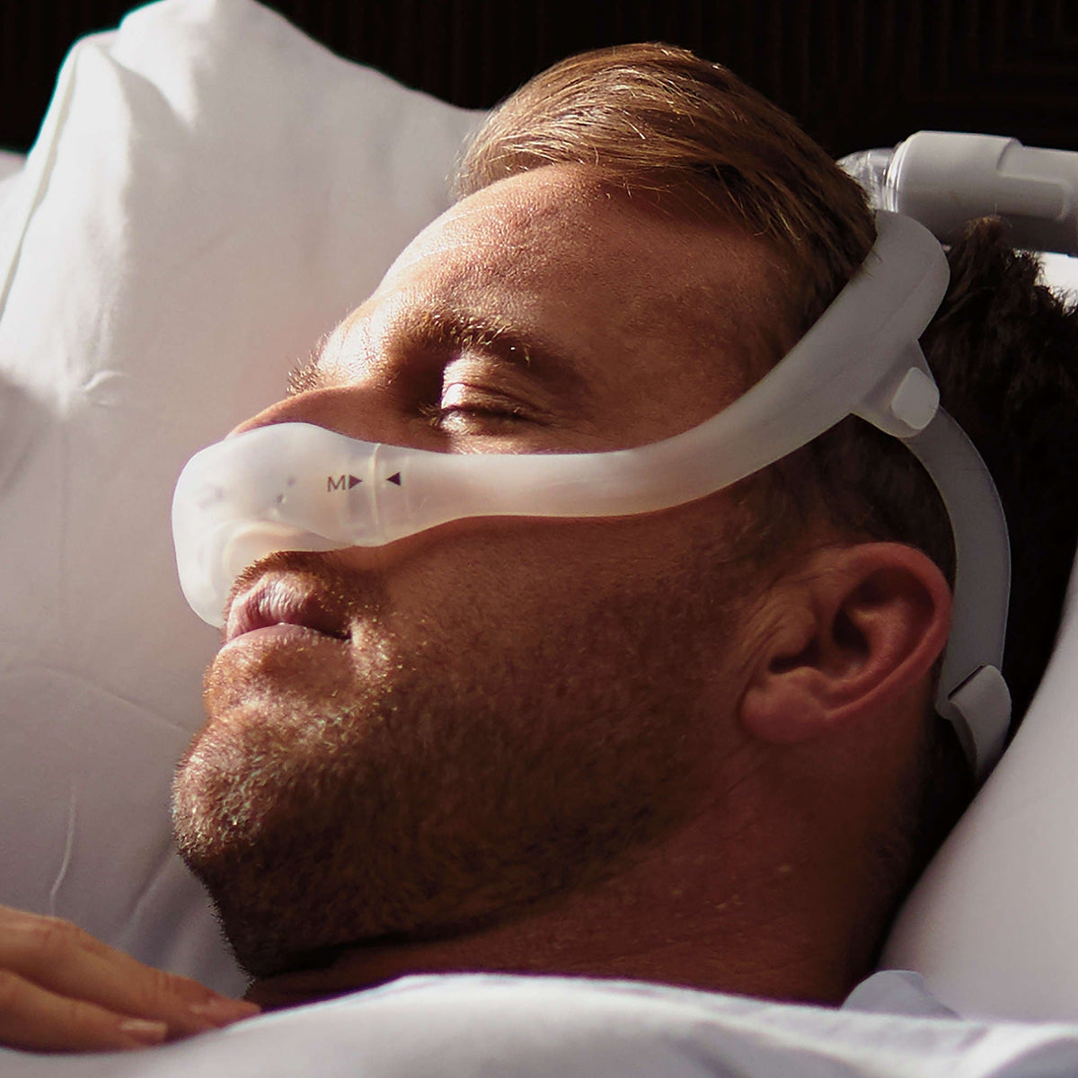 Sleeping man on a pillow in a DreamWear mask, seen up close, with the medium frame size mark visible