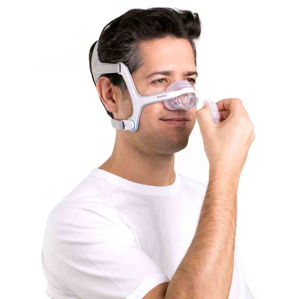 Man in a white t-shirt adjusting the AirFit N20 nasal mask over his nose, headgear in place