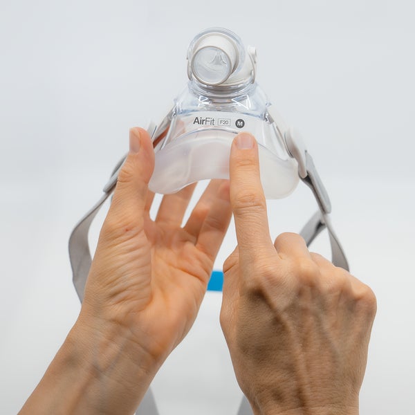 Hands pressing a new AirFit F20 cushion onto the mask frame, with the headgear still attached
