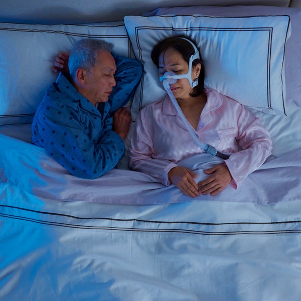 Photo of a woman asleep in the AirFit N20 For Her nasal mask while her partner sleeps beside her