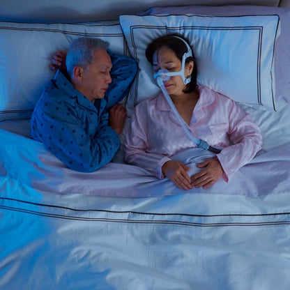 Photo of a woman asleep in the AirFit N20 For Her nasal mask while her partner sleeps beside her