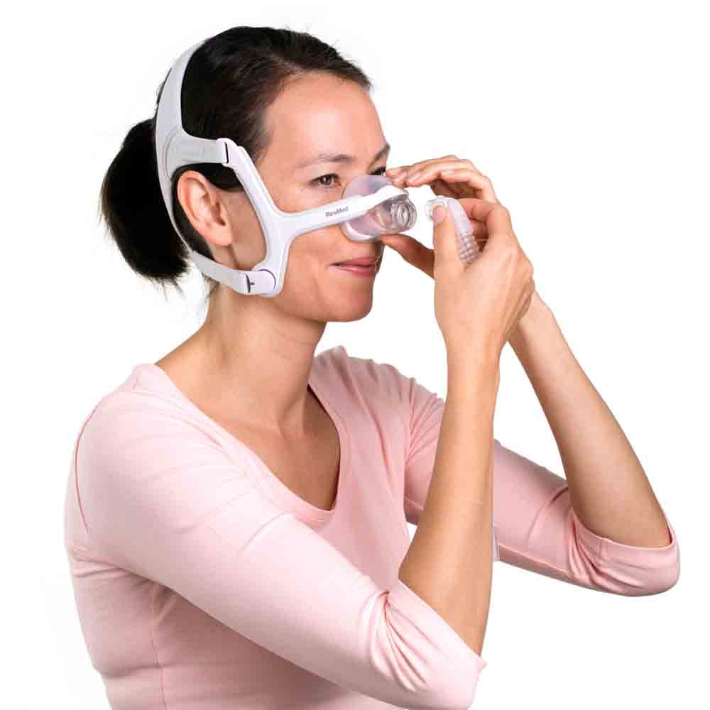 Photo of a woman holding the AirFit N20 For Her cushion to her nose while fitting the headgear