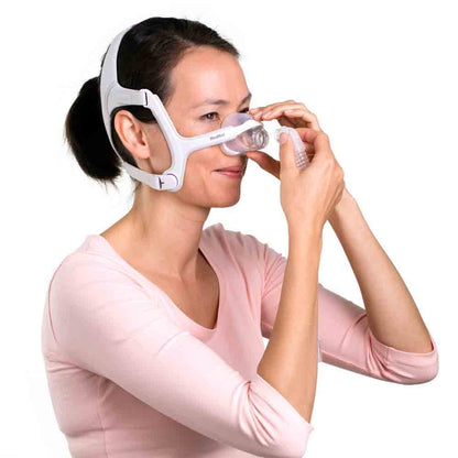 Photo of a woman holding the AirFit N20 For Her cushion to her nose while fitting the headgear