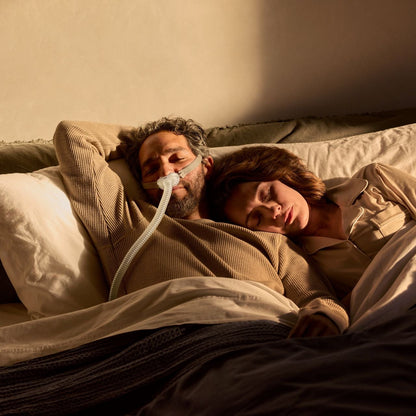 Photo of a man asleep in bed in the AirFit P10, with his partner resting her head on his shoulder