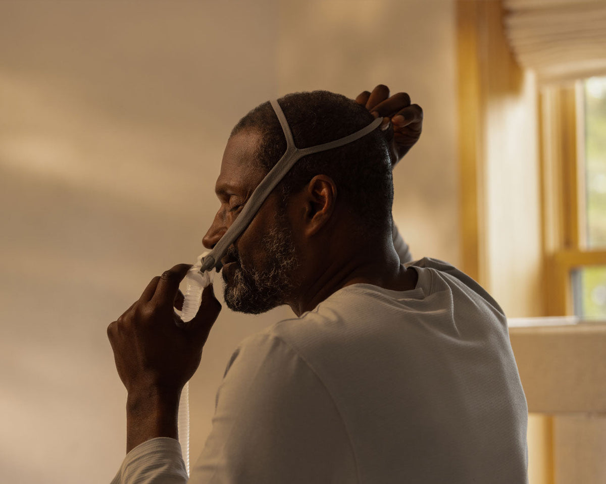 Photo of a man pulling the AirFit P10 headgear over his head while he holds the pillows in place