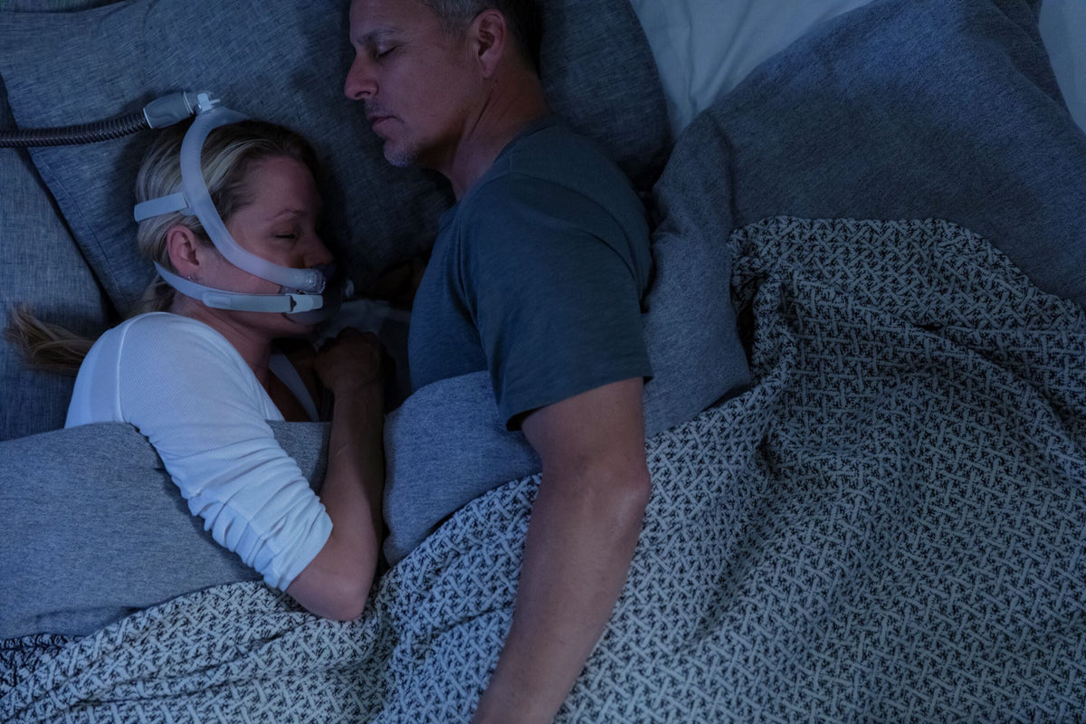 Photo of a woman asleep beside her partner, wearing the AirFit X30i with the hose running over her head