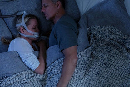 Photo of a woman asleep beside her partner, wearing the AirFit X30i with the hose running over her head