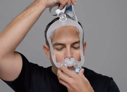 Photo of a man fitting the AirFit X30i, settling the pillows at his nostrils and the cushion over his mouth