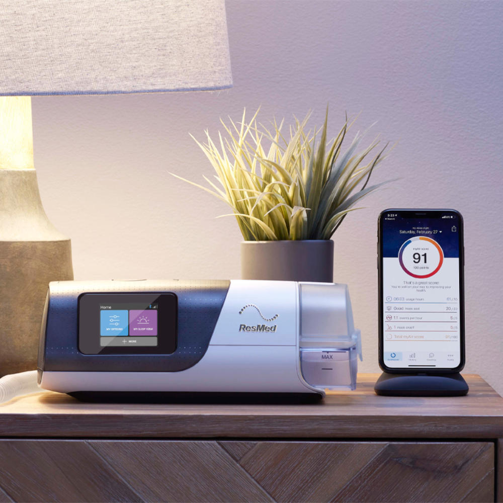 Bedroom nightstand holding an AirSense 11 with a HumidAir 11 tub at its end, a potted plant behind