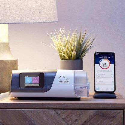 Bedroom nightstand holding an AirSense 11 with a HumidAir 11 tub at its end, a potted plant behind