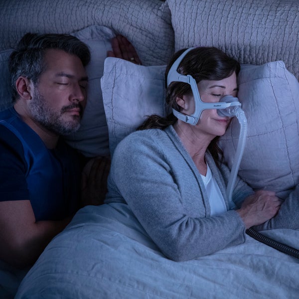 Photo of a woman asleep in the AirTouch N20 For Her nasal mask, with her partner sleeping beside her