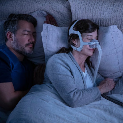 Photo of a woman asleep in the AirTouch N20 For Her nasal mask, with her partner sleeping beside her