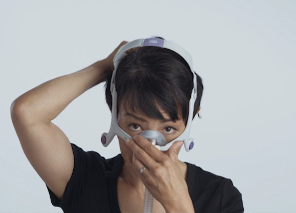Photo of a woman holding the AirTouch N20 For Her to her nose while pulling the headgear on