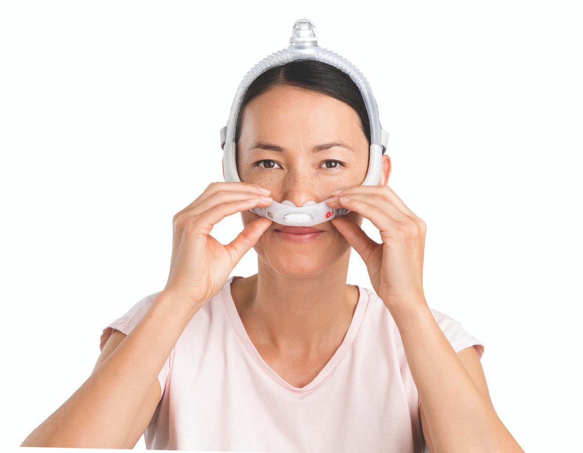 Photo of a woman settling the AirFit P30i pillows at her nostrils, wearing the Small frame