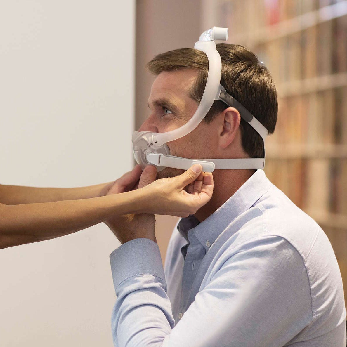A clinician steadying the cushion of the DreamWear Full Face mask on a seated man, seen from the side
