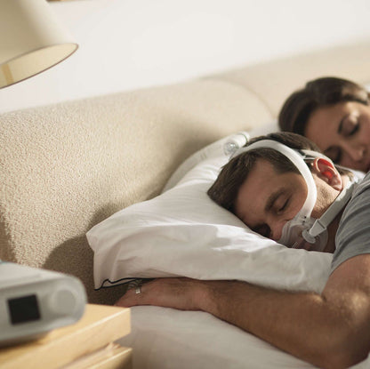 A man asleep on his side in the DreamWear Full Face mask, a bed partner beside him