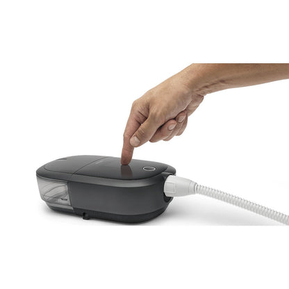 Angled view of the DreamStation 2 Auto CPAP Advanced as a hand taps the touchscreen, clear water tank at one end