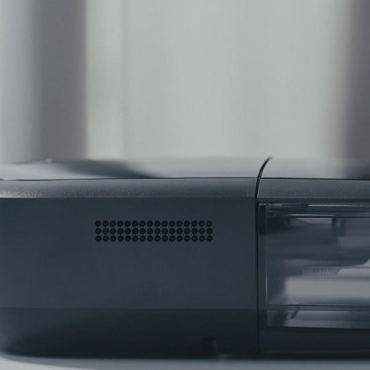Studio photo of the DreamStation 2 Auto CPAP Advanced from the side, showing the air vents and clear water tank