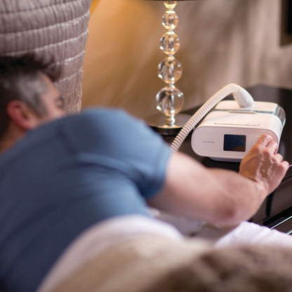 A man in bed reaching for the DreamStation Expert on his nightstand, its tube running to his mask