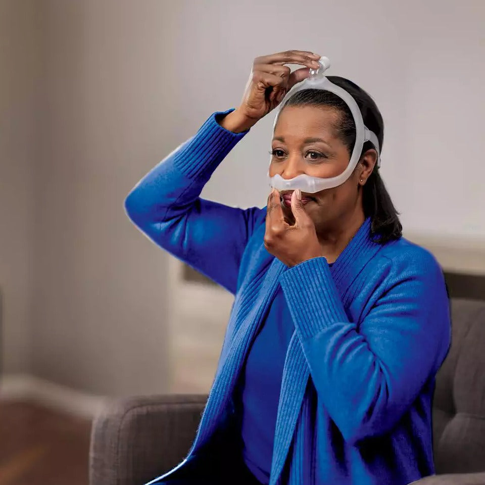 Woman wearing a DreamWear silicone pillows mask, adjusting it so the cushion sits at the base of her nose