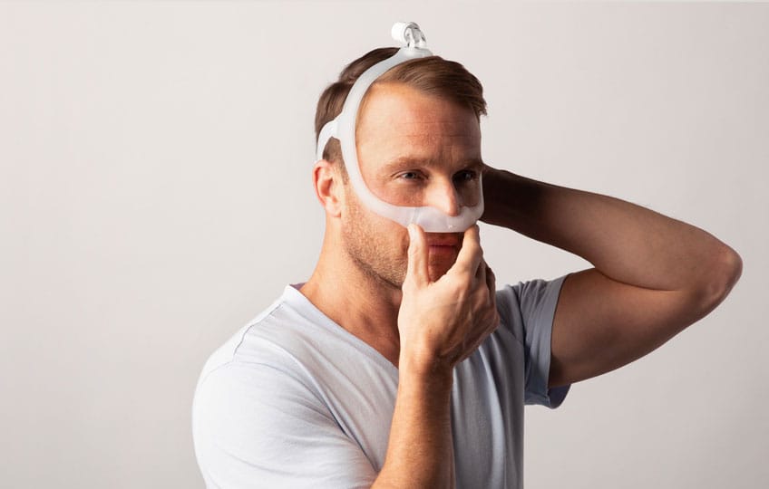 Photo of a man fitting the DreamWear Under the Nose, holding the cushion while adjusting the headgear
