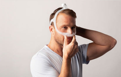 Photo of a man fitting the DreamWear Under the Nose, holding the cushion while adjusting the headgear