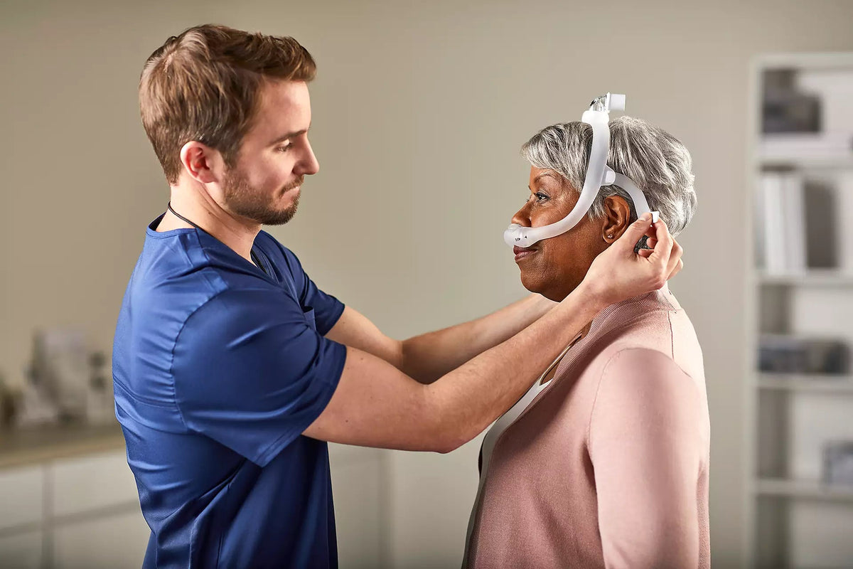 Photo of a clinician adjusting the DreamWear headgear on an older woman during a mask fitting