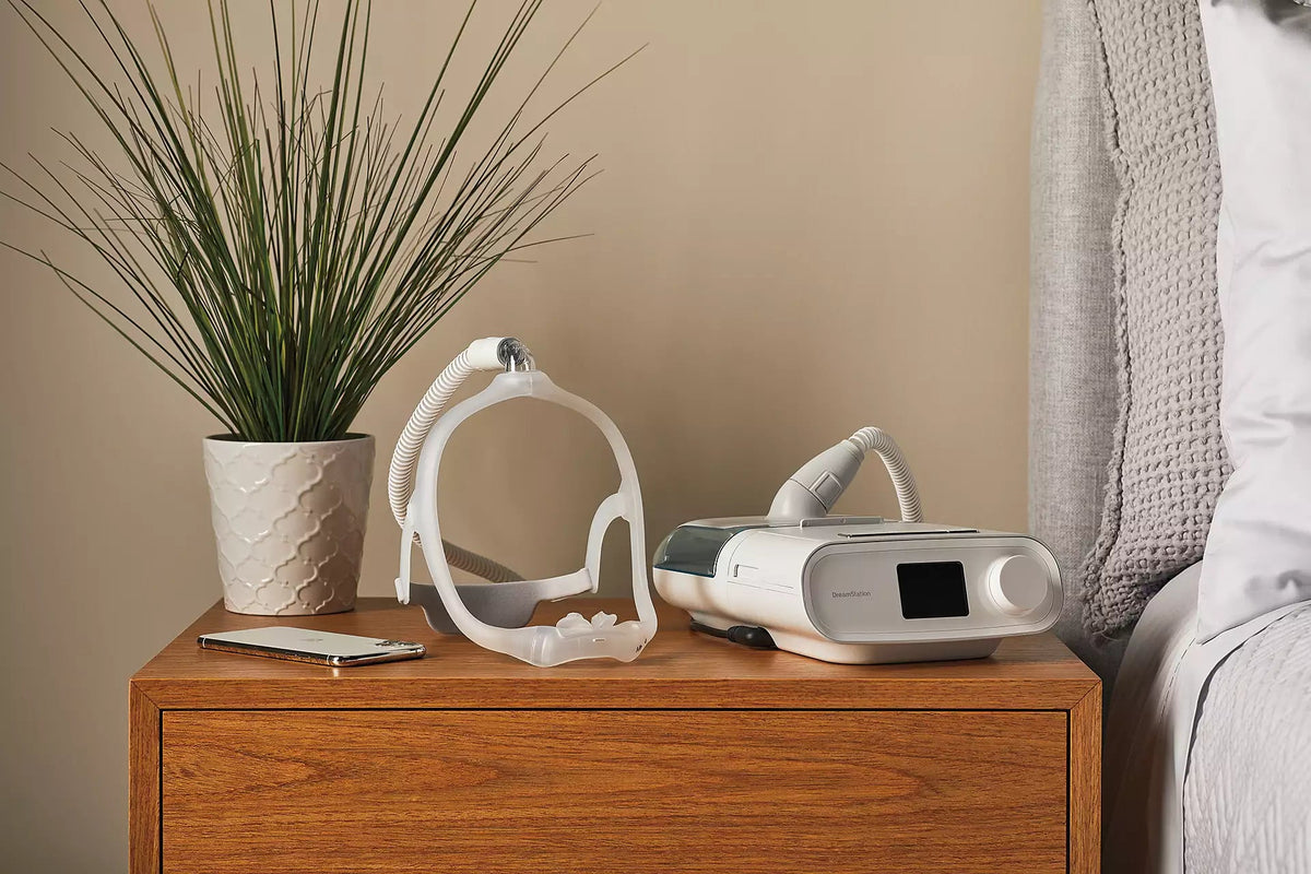 The DreamWear Silicone Pillows mask set down on a wooden nightstand, beside the machine it connects to