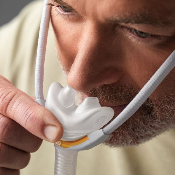 Fisher & Paykel Solo Nasal Pillow CPAP Mask cushion being held in place by a man with a beard to demonstrate the AutoFit seal.