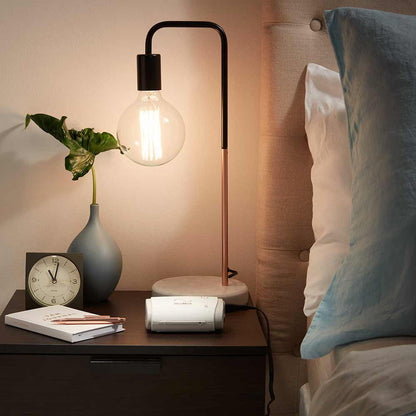 ResMed AirMini travel CPAP on a bedside table beside a lamp, a clock and a small plant
