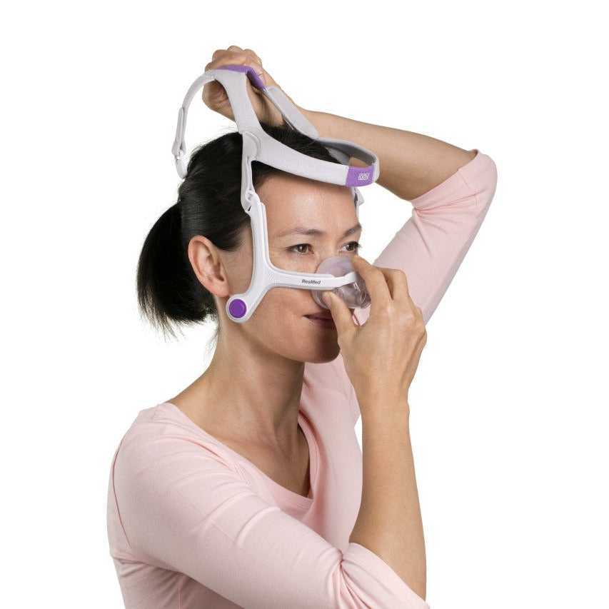 Woman holding the N20 For Her cushion to her nose with one hand while lifting the headgear over her head