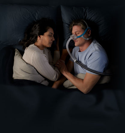 Photo of a man wearing the Nova Nasal in bed beside his partner, in a dim bedroom
