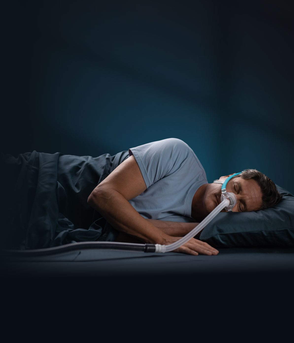 Photo of a man asleep on his side in the Nova Nasal mask, the hose running down past his shoulder