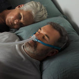 Photo of a man wearing the Nova Micro in bed on his back, his partner asleep beside him