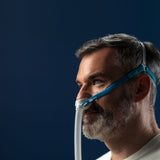 Side photo of a man wearing the Nova Micro, the pillows cushion at his nostrils and the tube hanging below