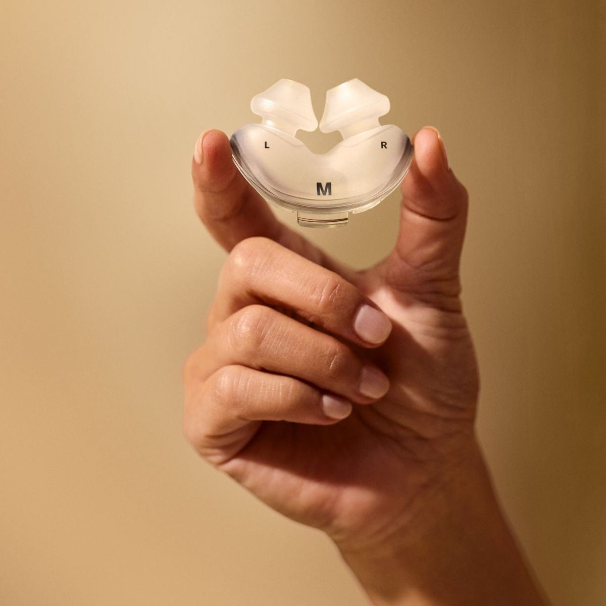 Hand holding a set of AirFit P10 nasal pillows up to the light to show the soft silicone