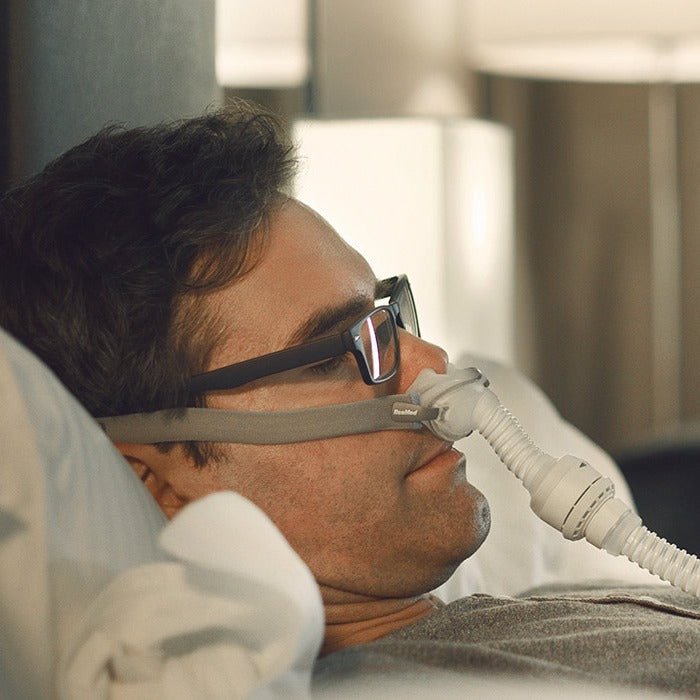Photo of a man in glasses reading his phone in bed while wearing the AirFit P10 for AirMini