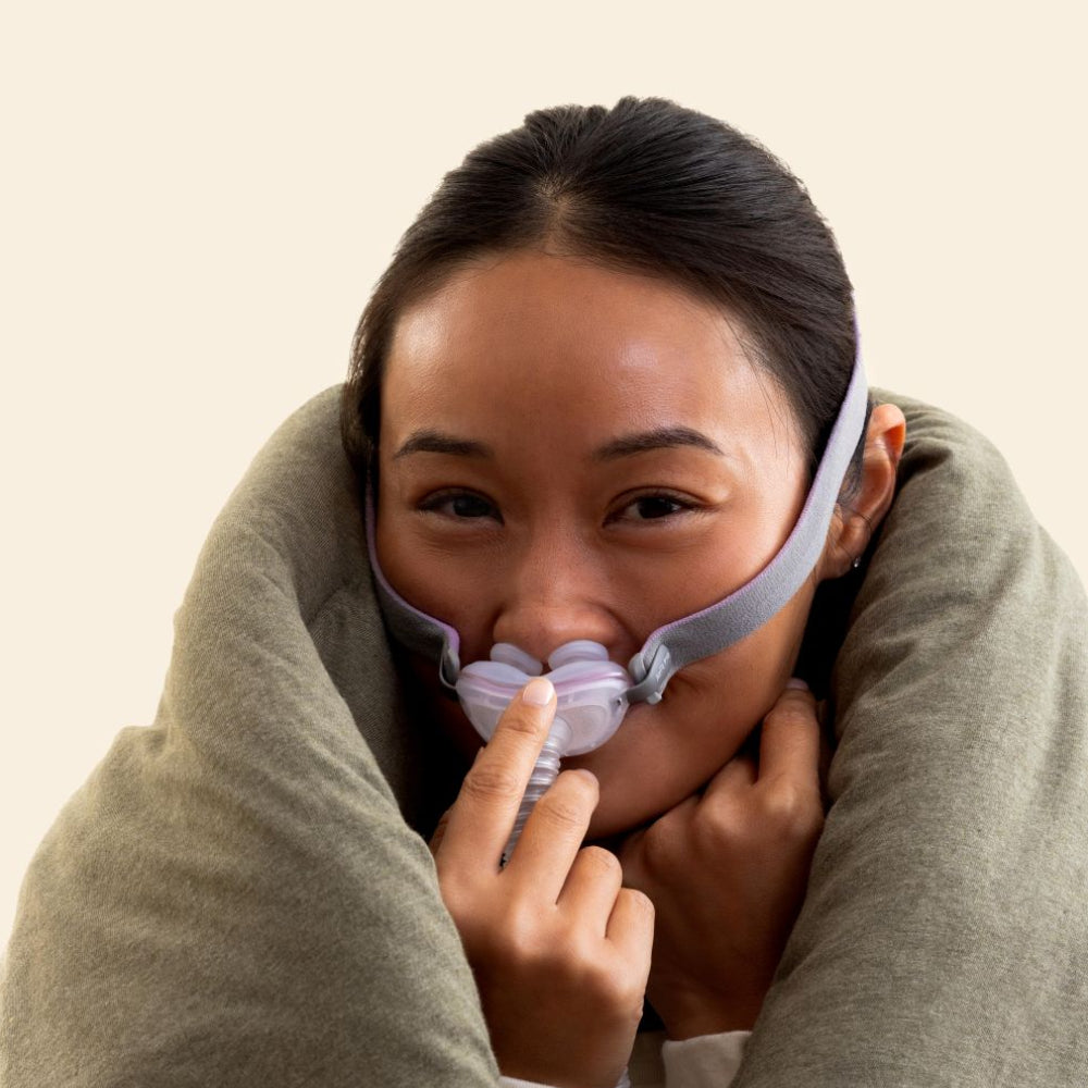 Photo of a woman wrapped in a blanket wearing the AirFit P10 For Her, smiling at the camera