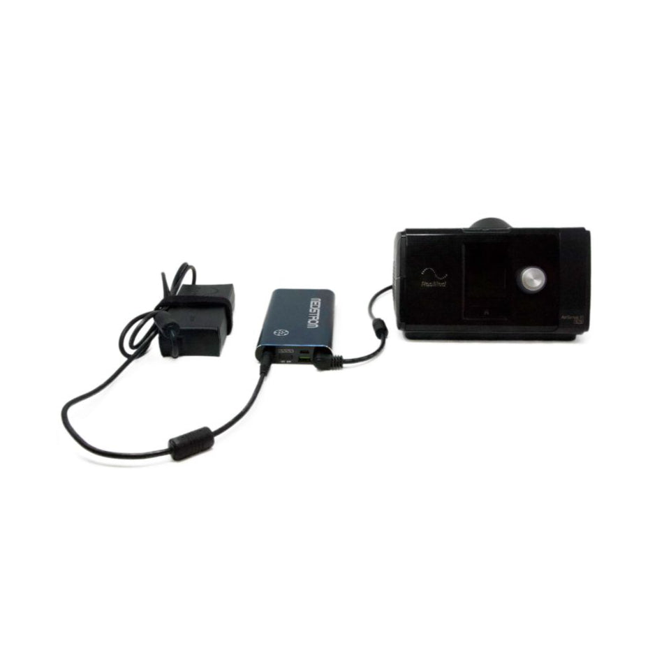 Angled view of the Pilot Flex battery in Dark Navy wired to a CPAP machine and its power adapter
