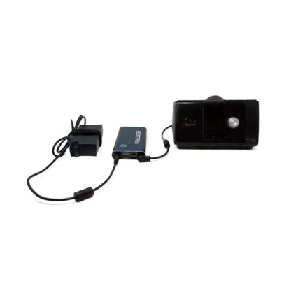 Angled view of the Pilot Flex battery in Dark Navy wired to a CPAP machine and its power adapter