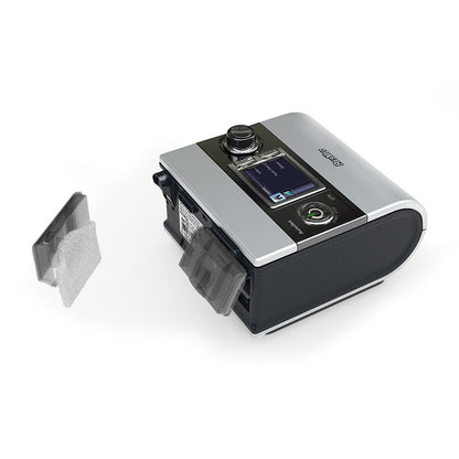 Photo of a ResMed S9 with its air filter cover off and a standard filter pad shown beside it