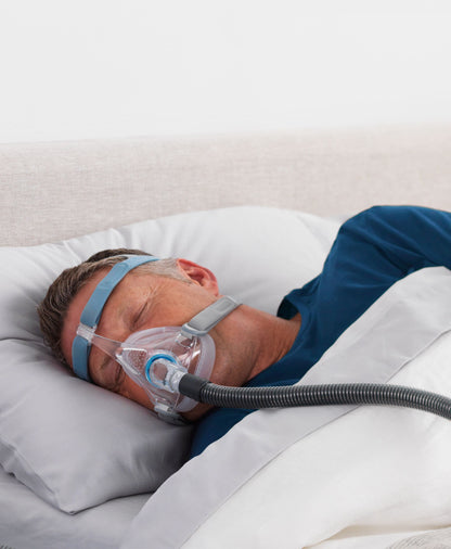 A man asleep on his side in the Vitera mask, its tube running across the pillow behind him